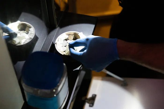 Person mit blauen Handschuhen sortiert Tabletten in einer Schale, daneben steht ein Medikamentenbehälter.
