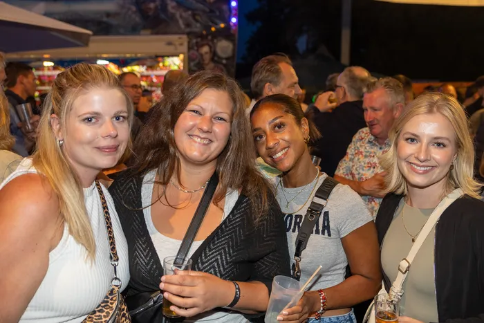 Vier lächelnde Frauen posieren bei der zehnten Q-Stall-Party inmitten einer Menschenmenge.