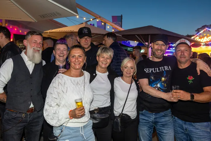 Eine Gruppe lächelnder Menschen posiert mit Getränken bei einer Abendveranstaltung im Freien.
