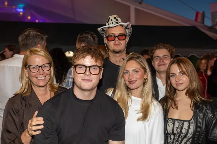 Eine Gruppe lächelnder Gäste posiert bei der zehnten Q-Stall-Party, darunter ein Mann mit Cowboyhut und roter Sonnenbrille.