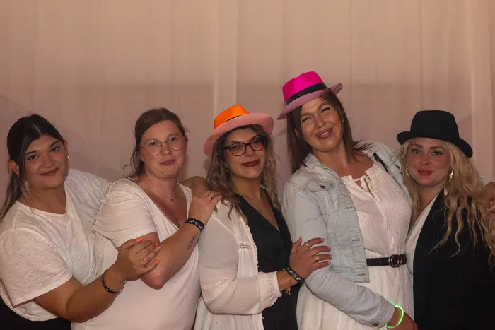 Fünf lächelnde Frauen posieren bei einer Party, einige tragen farbenfrohe Hüte in Orange, Pink und Schwarz.
