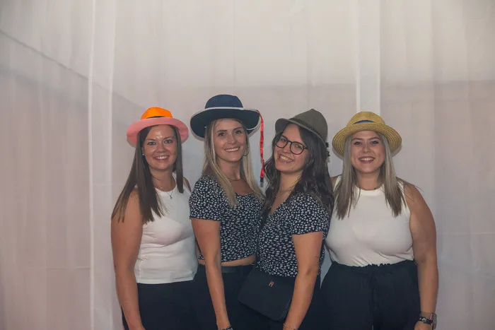 Vier lächelnde Frauen mit unterschiedlichen Sommerhüten posieren vor einem weißen Hintergrund.