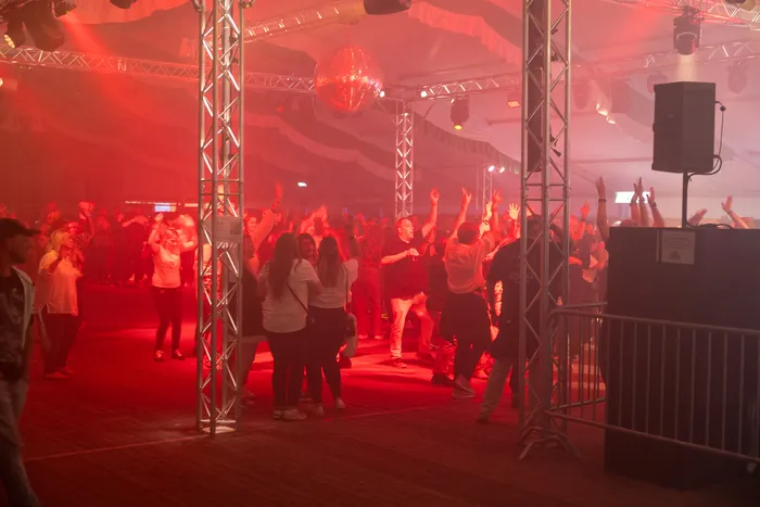 Menschen tanzen bei einer Party in einem Festzelt unter roter Beleuchtung und einer Discokugel.