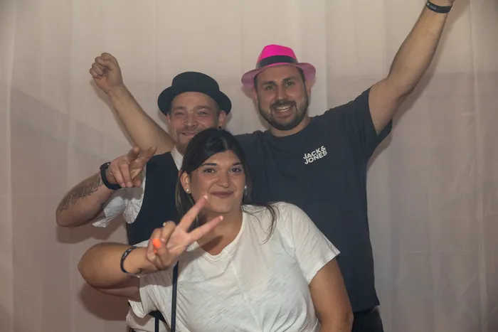 Drei Personen posieren mit Handzeichen vor einem hellen Hintergrund bei der Q-Stall-Party.