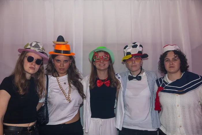 Fünf junge Frauen mit bunten Partyhüten und Accessoires posieren vor einem weißen Vorhang.