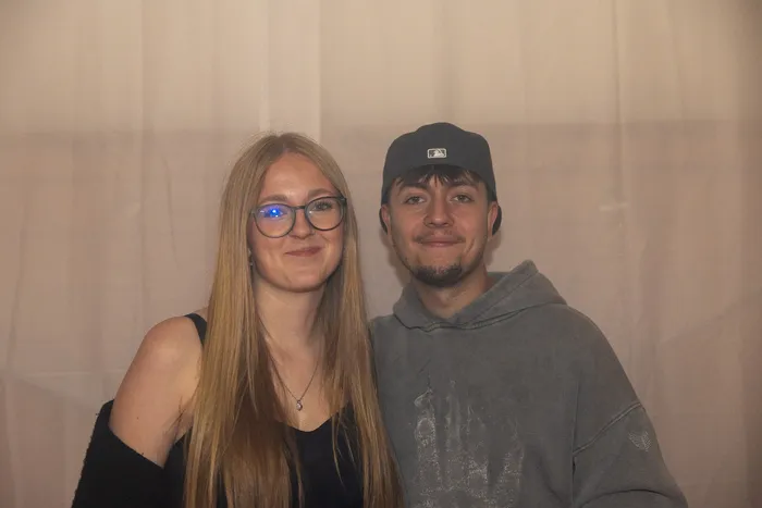 Eine junge Frau mit Brille und ein junger Mann mit grauer Kappe lächeln in die Kamera.