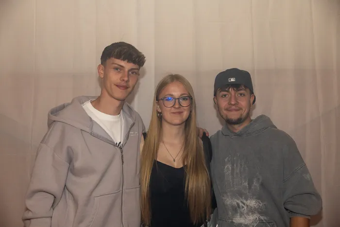 Drei junge Menschen posieren nebeneinander vor einem weißen Vorhang.