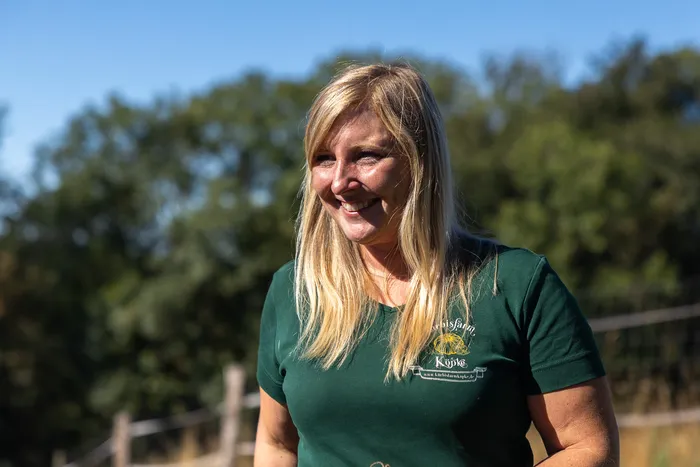 Eine lächelnde blonde Frau trägt ein grünes T-Shirt mit dem Aufdruck „Köpke“.