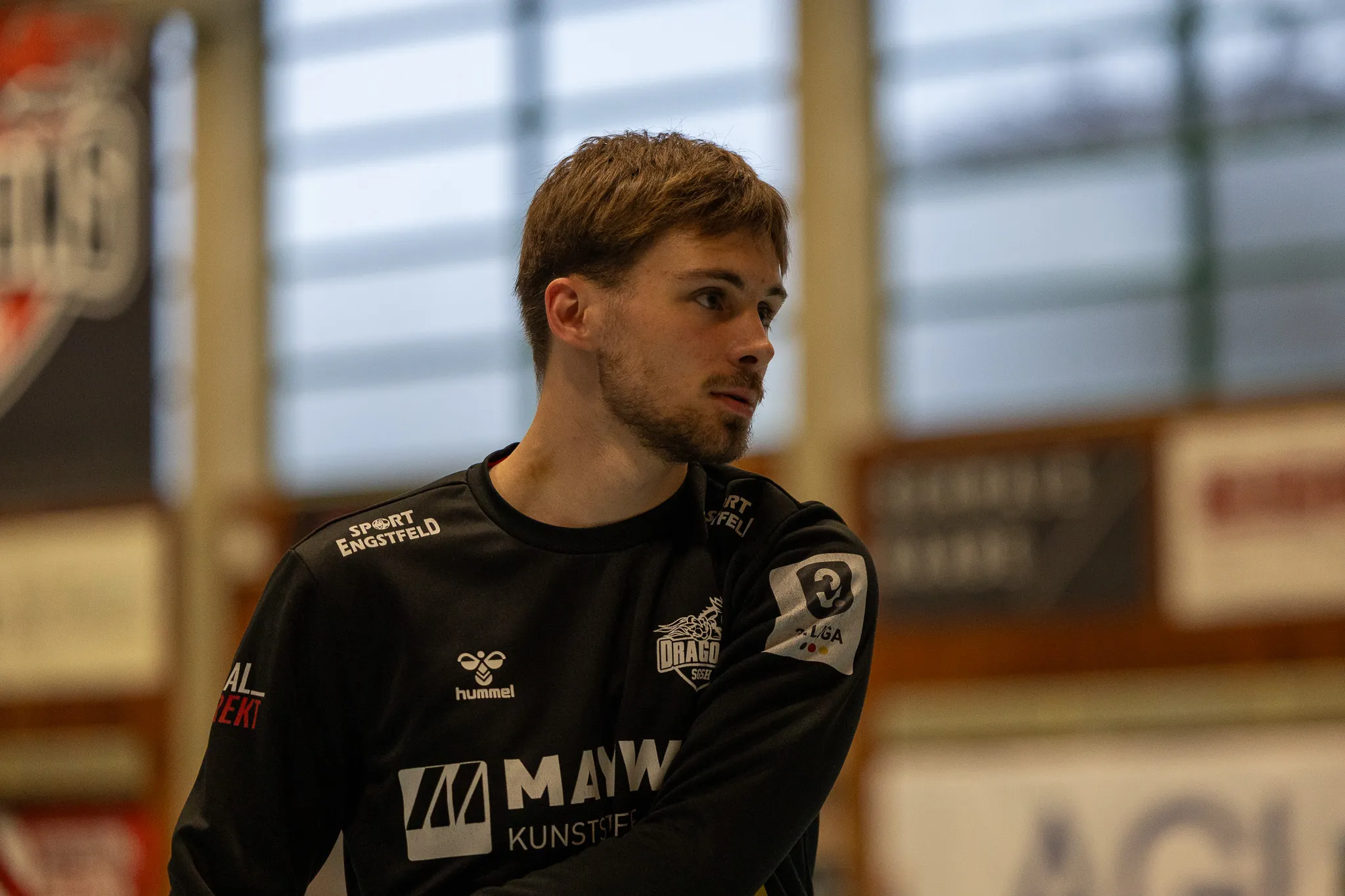 Handballspieler mit kurzem, braunem Haar und Bart in dunklem Trikot mit Werbeaufdruck beim Spiel.
