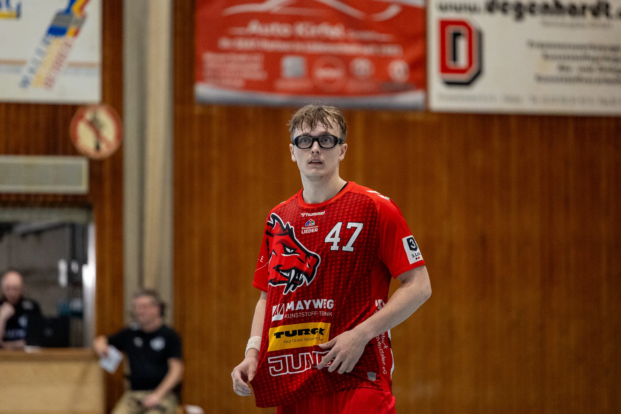Handballspieler mit der Trikotnummer 47 der SGSH Dragons steht auf dem Spielfeld und hält einen Ball. Im Hintergrund ist ein Werbebanner zu sehen.