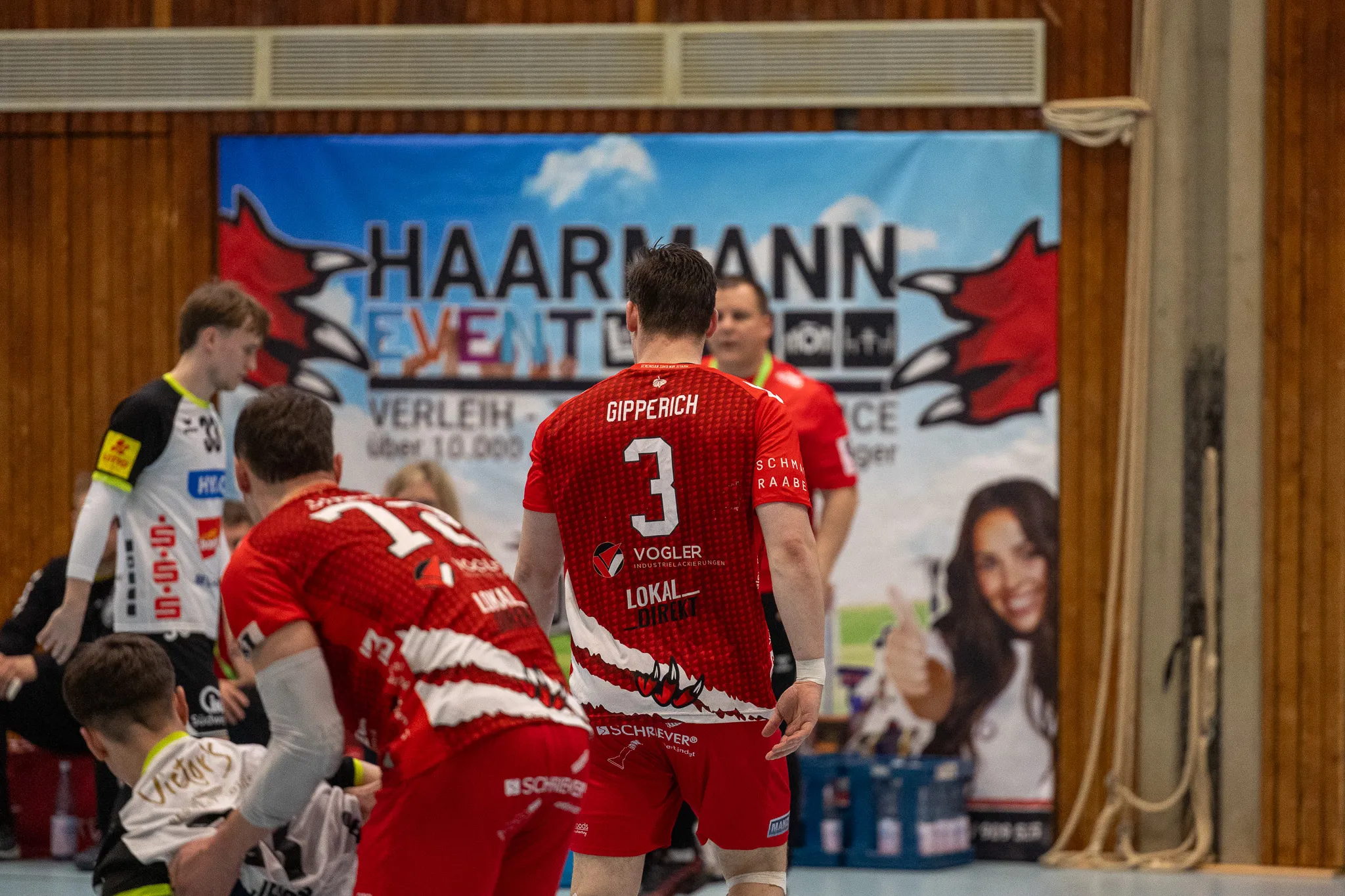 Handballspieler mit der Rückennummer 3 steht dem Betrachter zugekehrt in einer Sporthalle, im Hintergrund ein Banner mit der Aufschrift „HAARMANN EVENTS“.