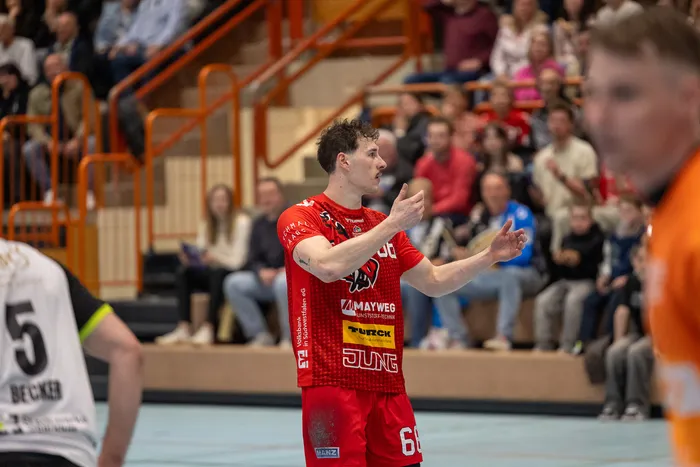 Handballspieler in rotem Trikot mit der Nummer 66 gestikuliert während des Spiels auf dem Spielfeld, im Hintergrund Zuschauer auf den Tribünen.