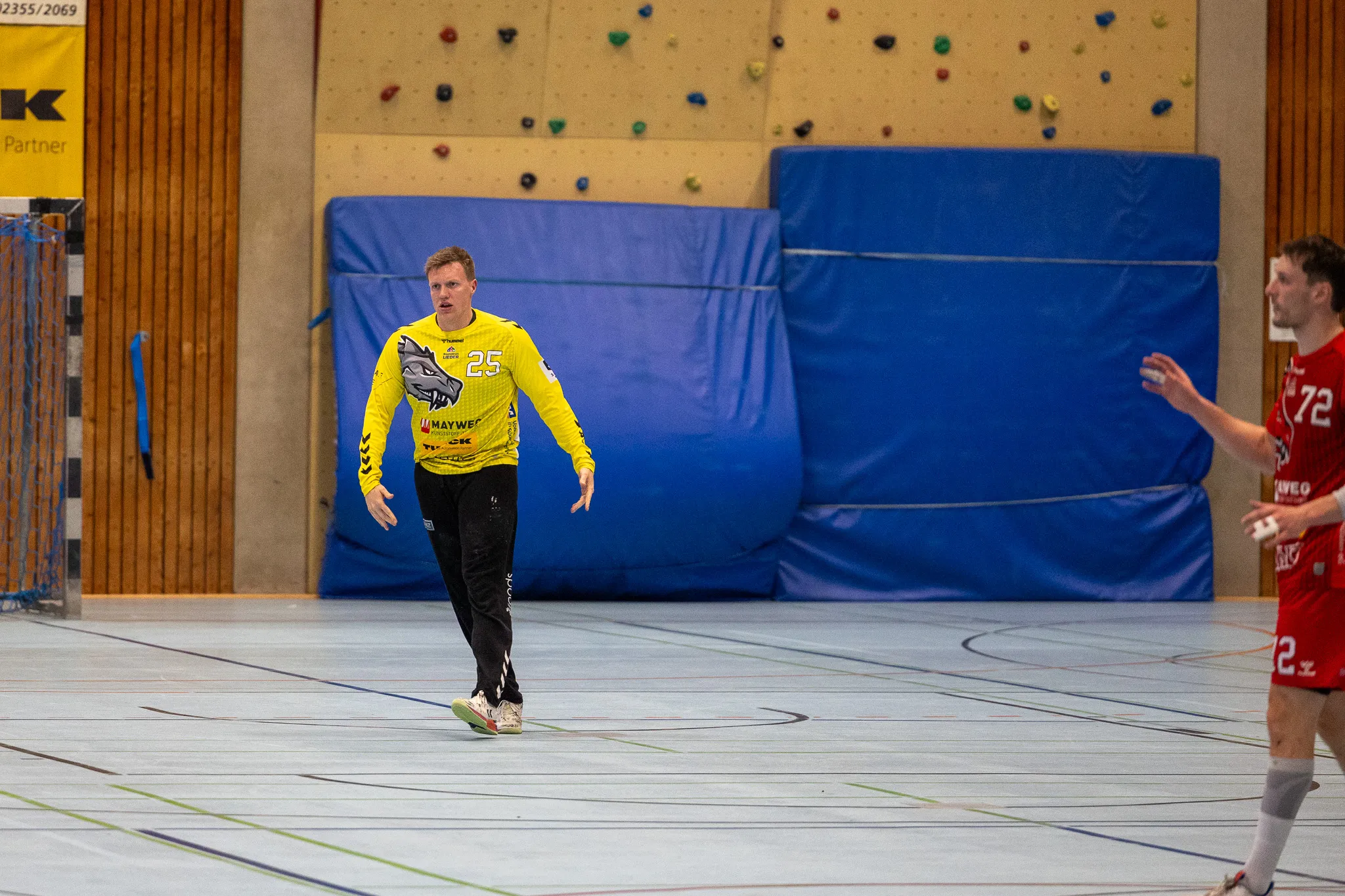 Handballspieler mit der Trikotnummer 25 geht auf das Tor zu, während ein Gegenspieler im Hintergrund verteidigt.