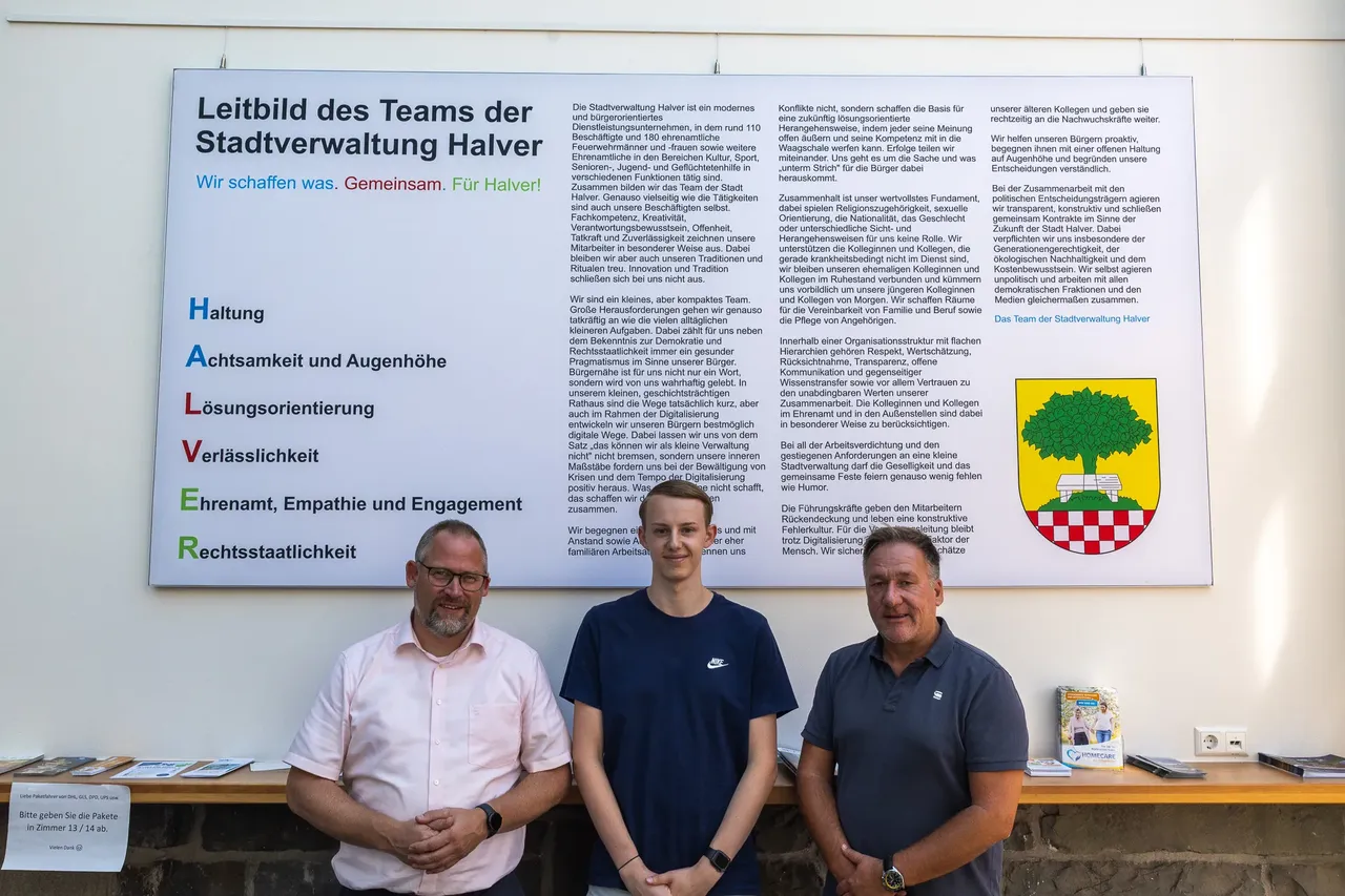 Bürgermeister Armin Kibbert, Azubi Julian Lenz und Kämmerer Simon Thienel stehen vor dem Leitbild der Stadtverwaltung Halver.