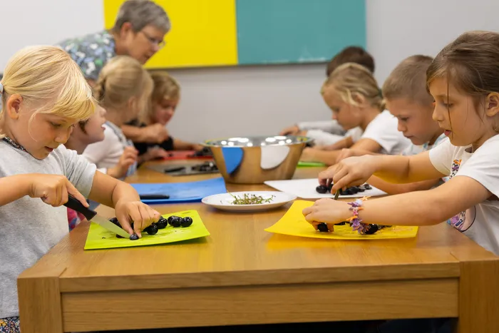 Kinder schneiden dunkle Früchte auf bunten Schneidebrettern an einem Holztisch.