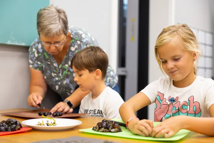 Eine Frau hilft zwei Kindern beim Anrichten von Weintrauben auf Tellern.