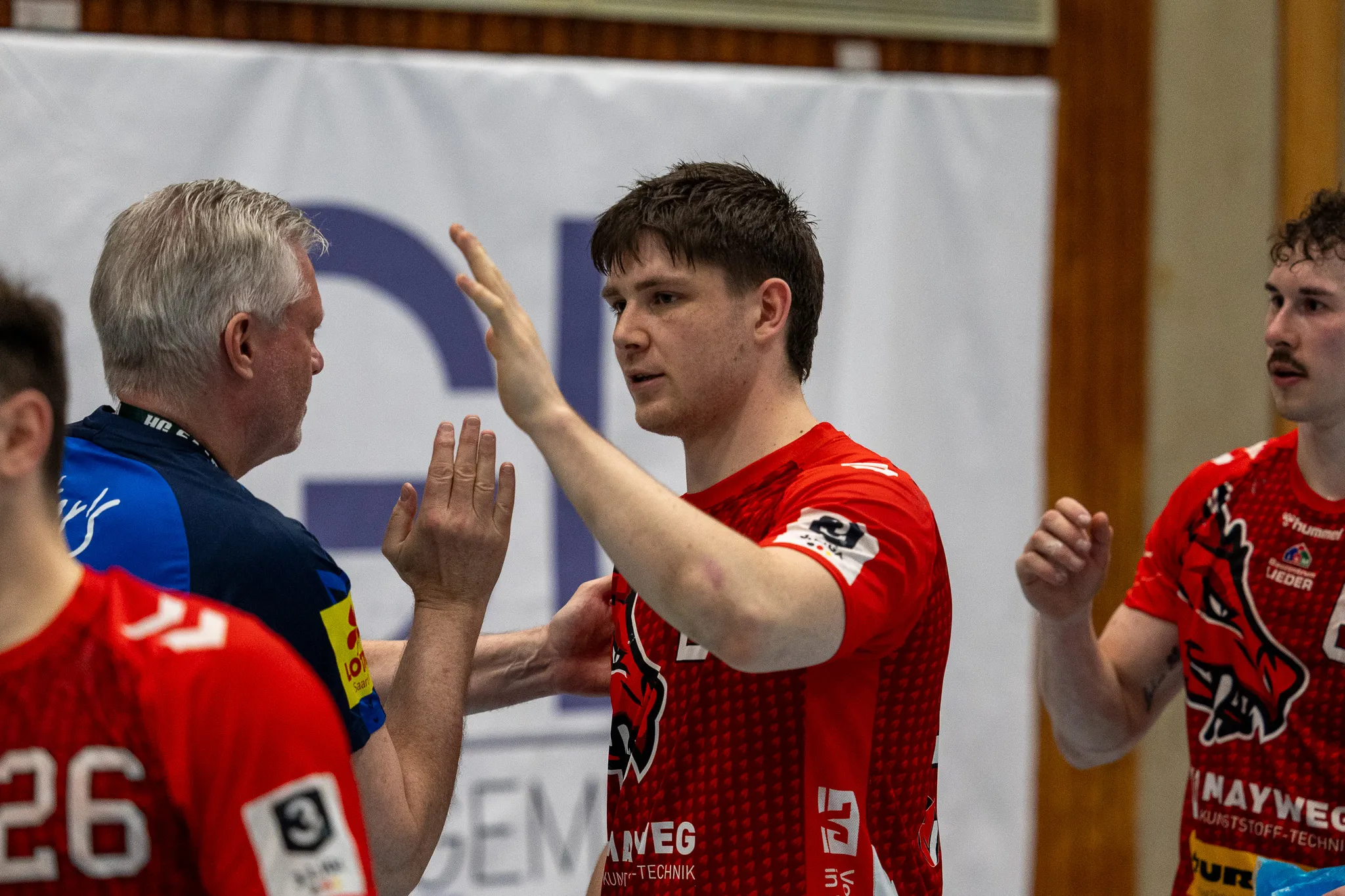 Zwei Handballspieler der SGSH Dragons und ein Schiedsrichter diskutieren während eines Spiels. Der Schiedsrichter gestikuliert mit erhobener Hand.