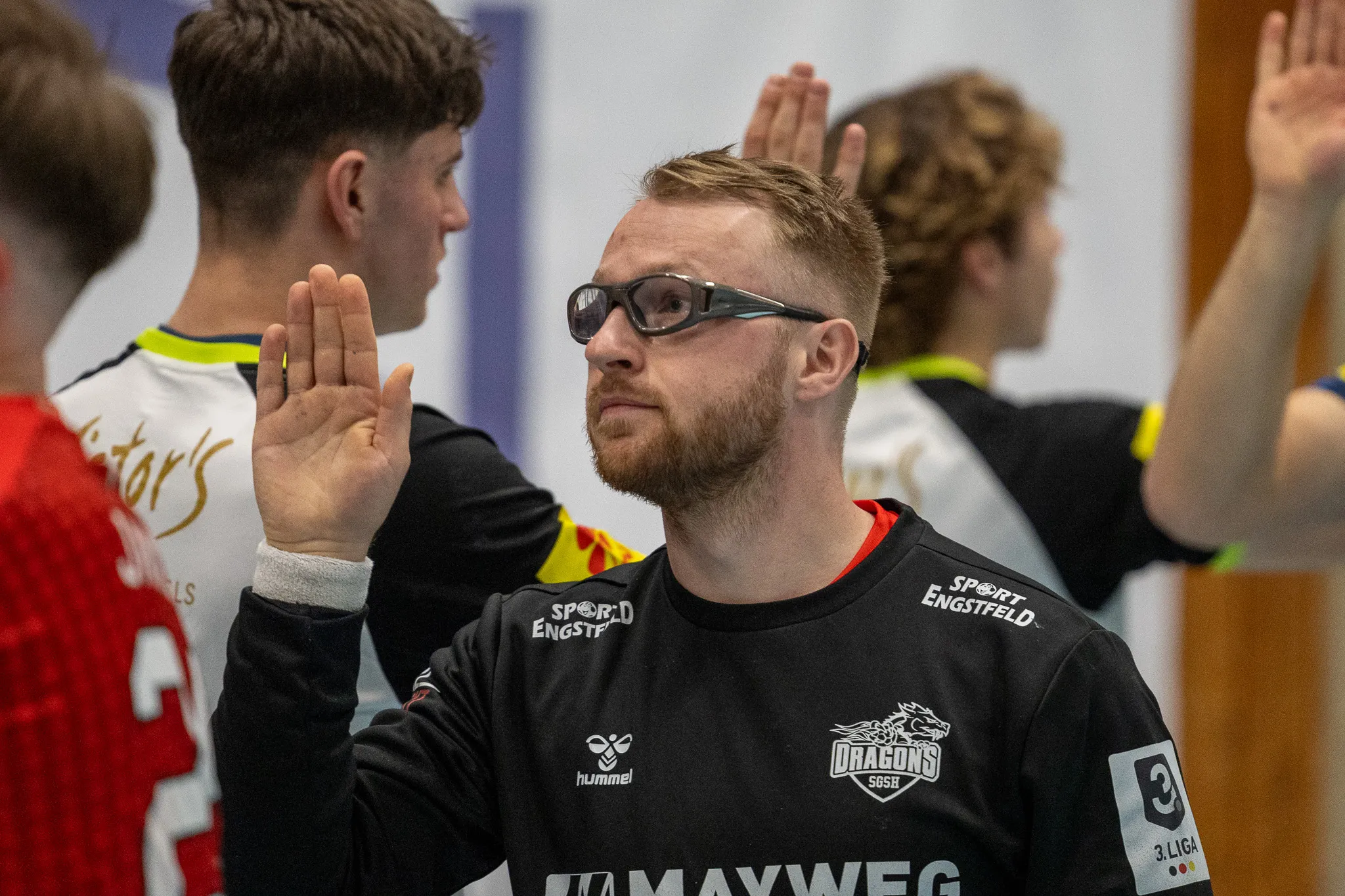 Handballspieler mit Brille und hoch erhobenen Händen, trägt Trikot der SGSH Dragons mit dem Aufdruck „Sport Engstfeld“ und „3. Liga“.