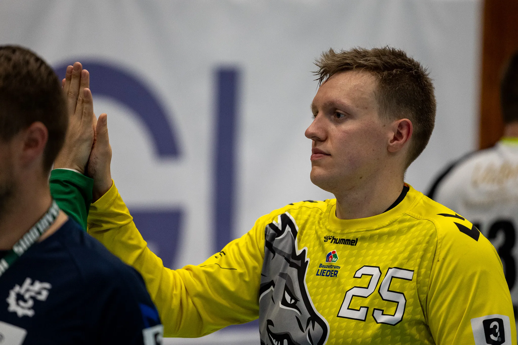 Handballspieler mit blonden Haaren in gelbem Trikot mit der Nummer 25 gibt einem Gegenspieler mit grünem Trikot einen High Five.