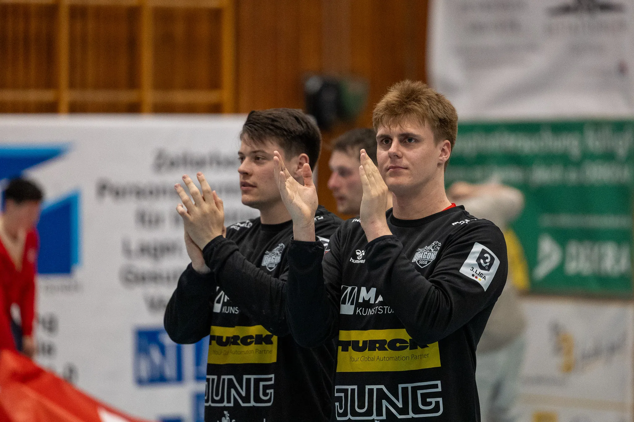 Handballspieler der SGSH Dragons klatschen sich nach einem Spiel in der Halle zu. Auf ihren Trikots ist der Sponsor Turck zu sehen.