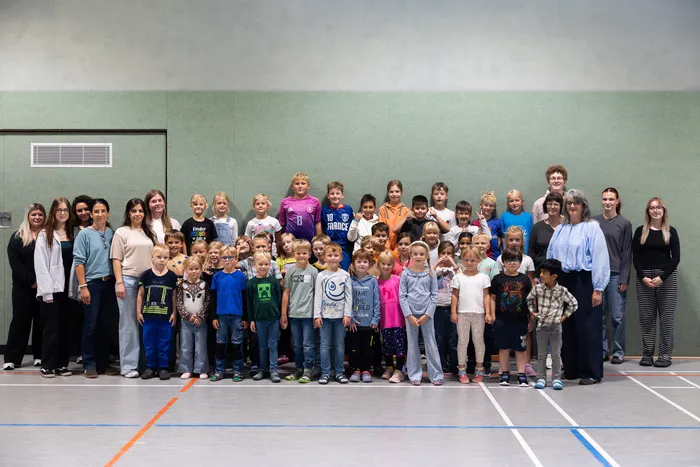 Eine große Gruppe von Kindern und Erwachsenen posiert für ein Gruppenfoto in einer Sporthalle.