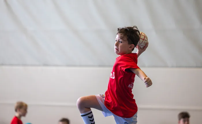 Ein Junge in einem roten T-Shirt und weißen Shorts springt mit einem Ball in der Hand bereit zum Wurf.