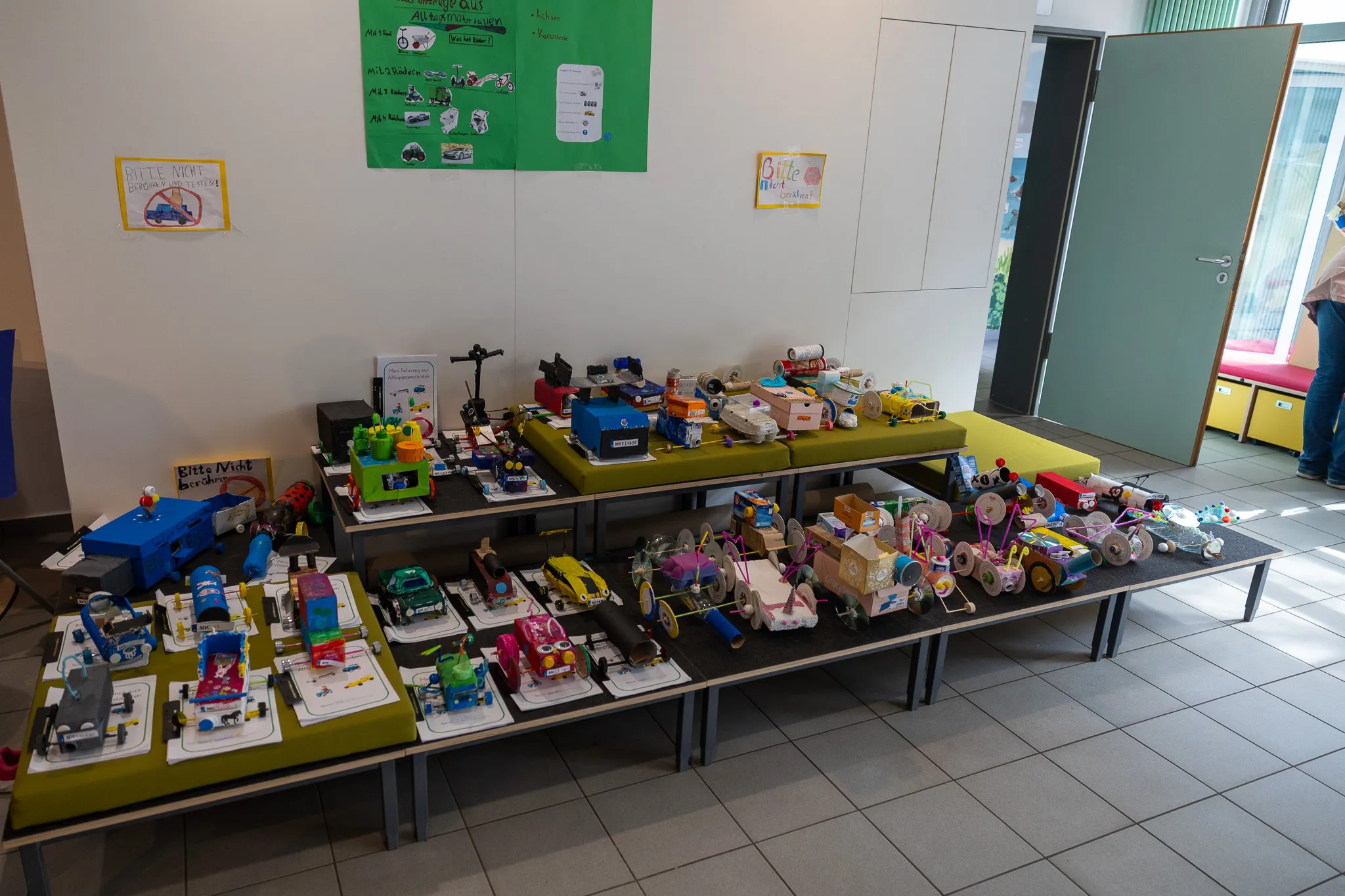 Ausstellung von Spielzeugfahrzeugen und -konstruktionen auf Tischen, erstellt von Schülern im Rahmen eines Lernprojekts.