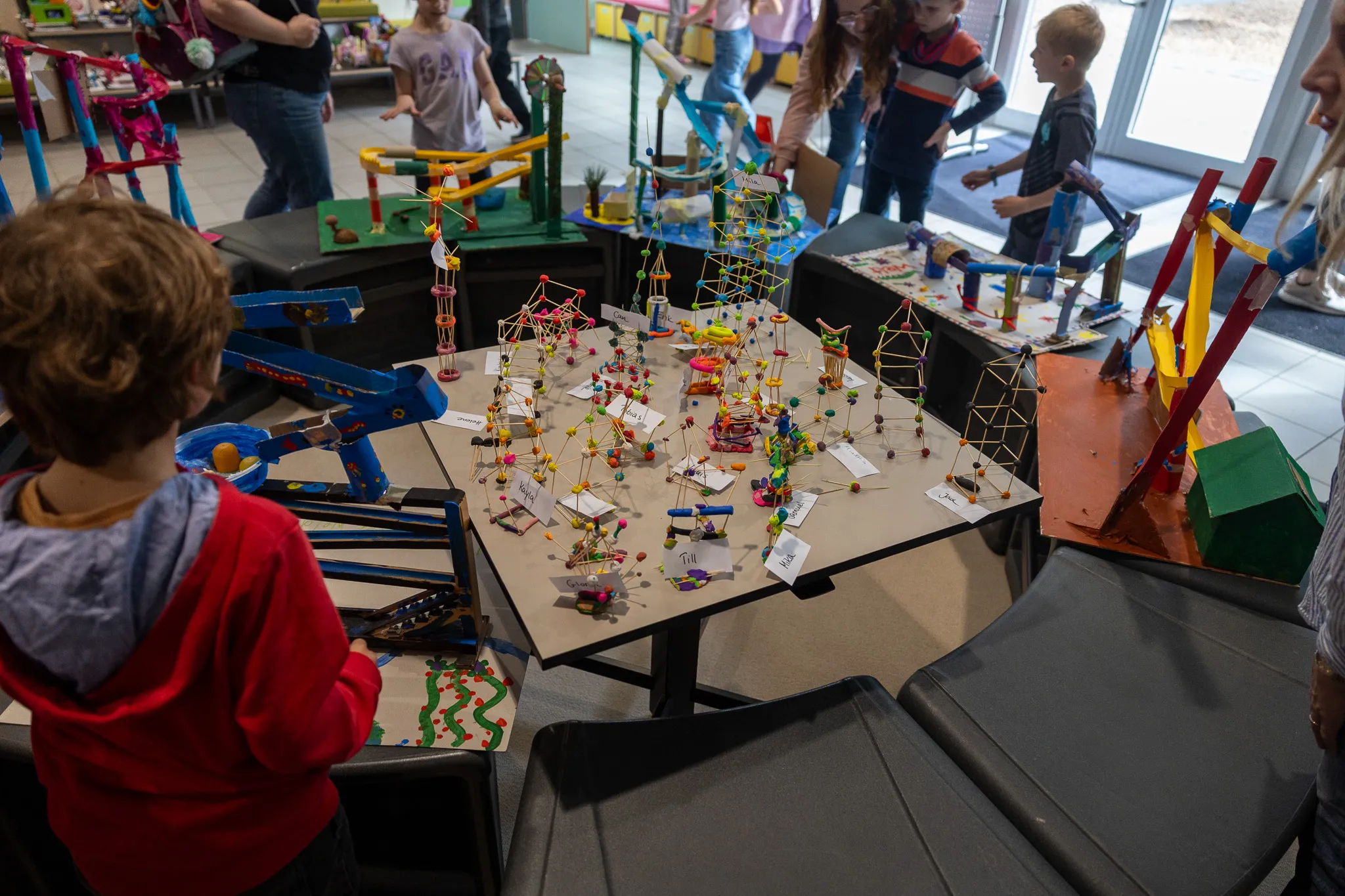Komplexe Konstruktion aus Holzstäben und Verbindern auf einem Tisch, umgeben von mehreren Murmelbahnen, die von Kindern gebaut wurden.