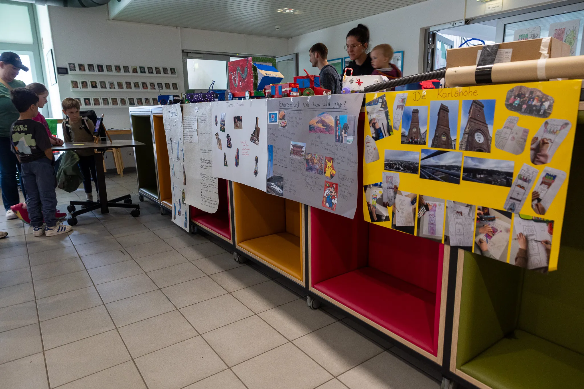 Schülerarbeiten zum Thema Bauen und Konstruieren sind auf Rollwagen in einem Flur ausgestellt, im Hintergrund stehen weitere Schüler und ein Erwachsener.