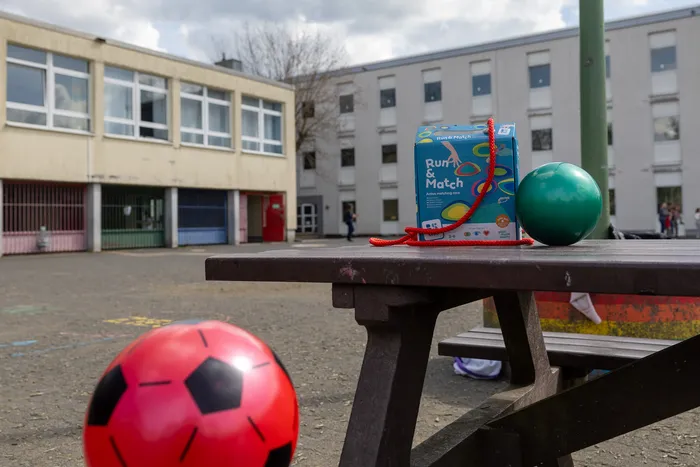 Spielzeug auf einem Picknicktisch im Schulhof: ein Fußball, ein grüner Ball und eine Spielzeugbox mit dem Aufdruck „Run & Match“.