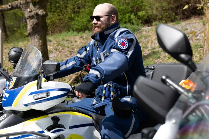 Ein Polizist mit Bart und Sonnenbrille sitzt auf einer gelben Motorrad, gekleidet in einer blauen Uniform mit Abzeichen und reflektierenden Streifen.