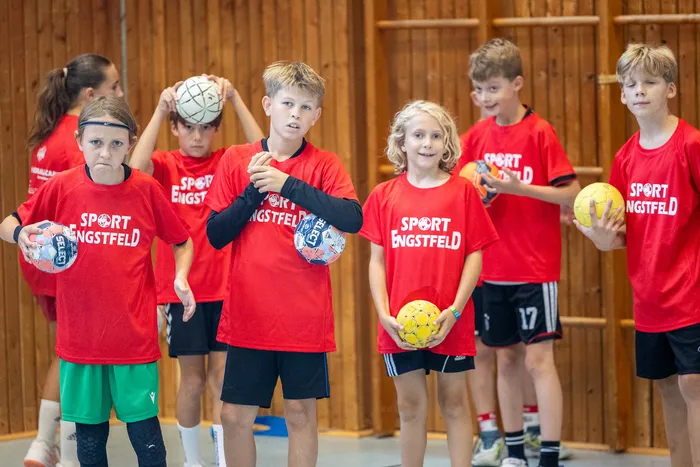 Kinder in roten T-Shirts mit der Aufschrift „SPORT ENGSTFELD“ halten bunte Bälle in einer Sporthalle.