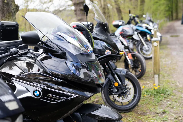 Mehrere Motorräder, darunter eine BMW K1300GT mit dem Logo der Bundespolizei, stehen auf einem Parkplatz am Waldrand.