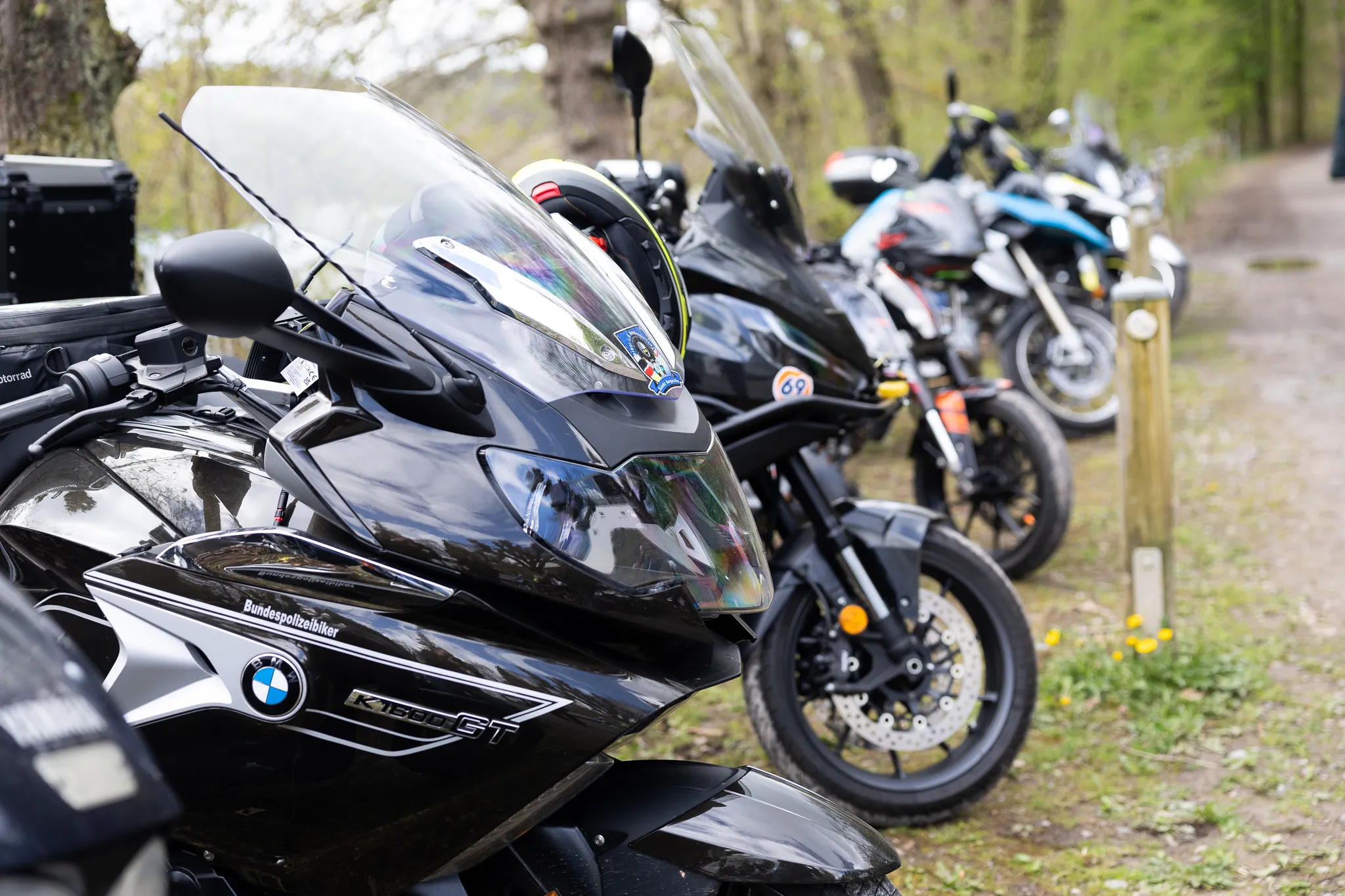 Mehrere Motorräder, darunter eine BMW K1300GT mit dem Logo der Bundespolizei, stehen auf einem Parkplatz am Waldrand.