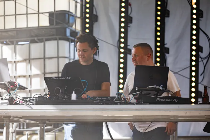 Vincent Sonore und JP Lekic bedienen DJ-Equipment und Laptops vor vertikalen Lichtleisten.