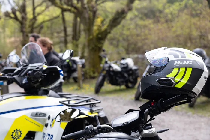 Motorradhelm mit gelben Streifen liegt auf dem Tank eines Polizeimotorrads, im Hintergrund weitere Motorräder und Polizisten.