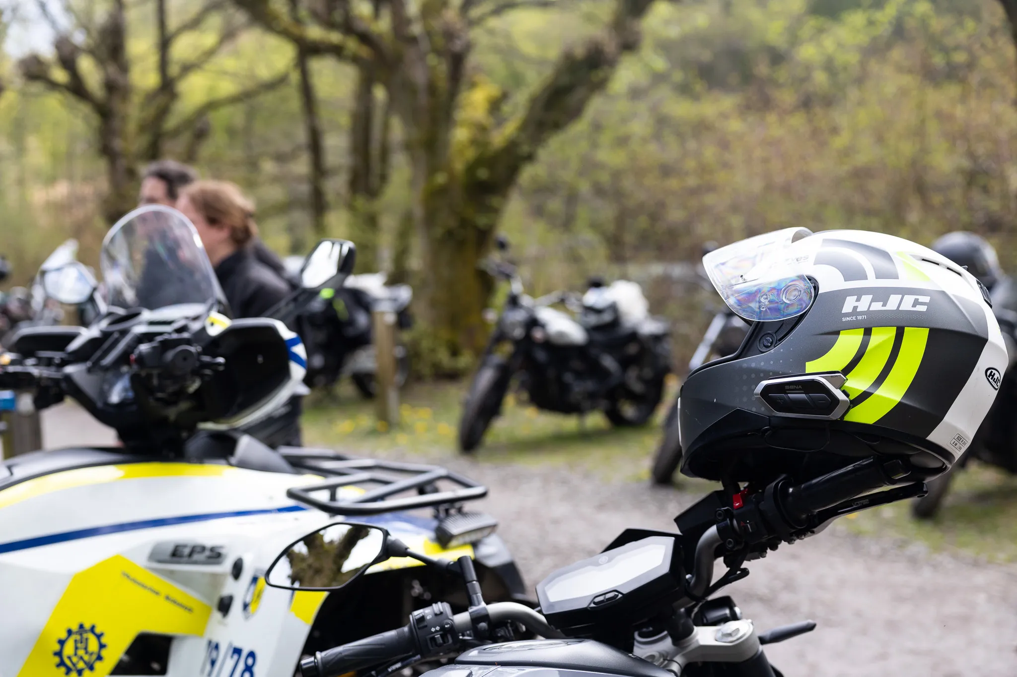 Motorradhelm mit gelben Streifen liegt auf dem Tank eines Polizeimotorrads, im Hintergrund weitere Motorräder und Polizisten.