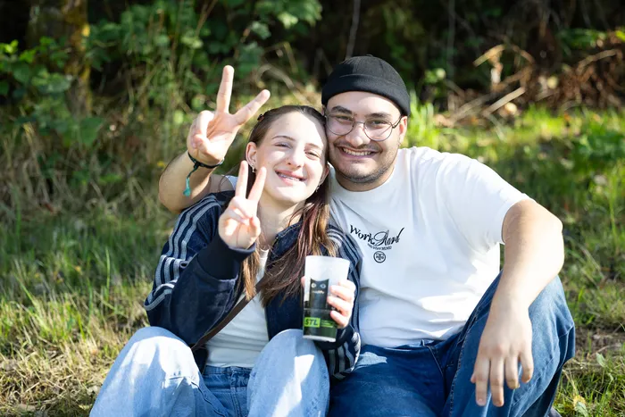 Vincent Sonore und JP Lekic sitzen lächelnd auf einer Wiese vor einem Waldhintergrund.