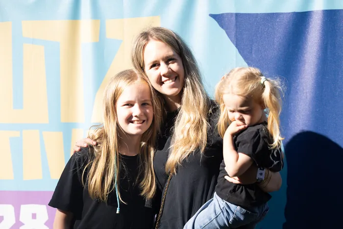 Eine lächelnde Frau mit zwei jungen Mädchen vor einem blau-gelben Banner.