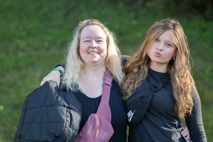 Eine blonde Frau und ein Mädchen mit langen, welligen Haaren posieren gemeinsam vor einem grünen Hintergrund.