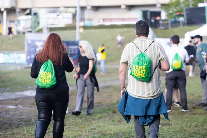 Personen laufen über ein Gelände und tragen grüne Beutel mit der Aufschrift „HOME SWEET HOME 2026“.