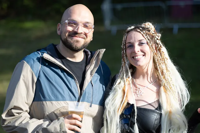 Vincent Sonore und JP Lekic lächeln in die Kamera. Der Mann hält ein Glas Bier, die Frau hat langes, blondes, geflochtenes Haar.