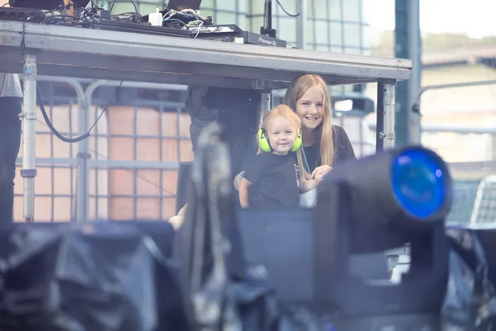 Zwei lächelnde Kinder stehen vor DJ-Equipment auf der Turntable Stage.