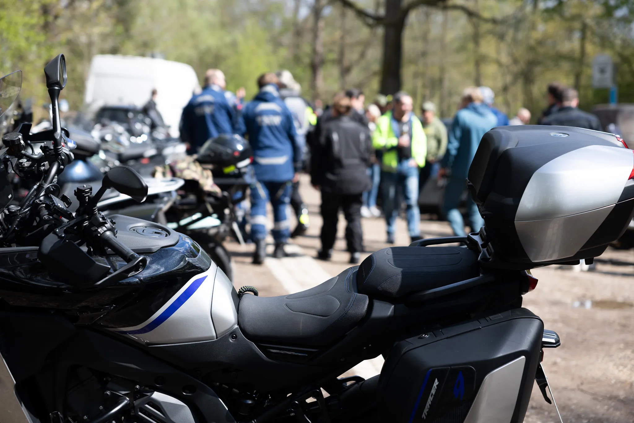 Motorräder stehen im Vordergrund, im Hintergrund eine Gruppe Menschen, darunter Polizisten in Uniform, bei einer Präventionsveranstaltung.