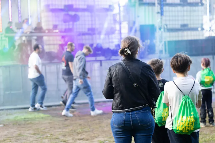 Eine Frau in einer schwarzen Jacke und zwei Kinder mit grünen Rucksäcken blicken auf die bunt beleuchtete Turntable Stage bei Bautz 2026.