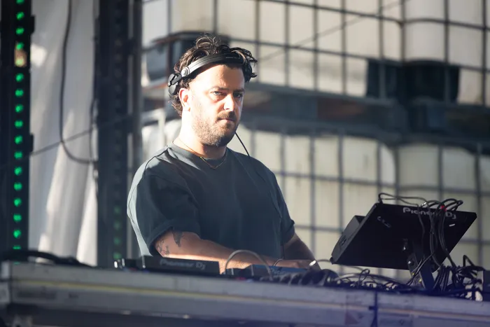 Disco Danny mit Kopfhörern hinter seinem DJ-Pult blickt in die Kamera.