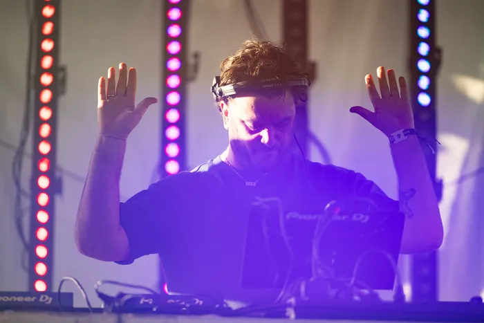 DJ Disco Danny mit erhobenen Händen hinter einem Mischpult unter violettem Bühnenlicht.
