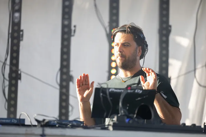 DJ Disco Danny mit Kopfhörern hinter einem Mischpult und erhobenen Händen.