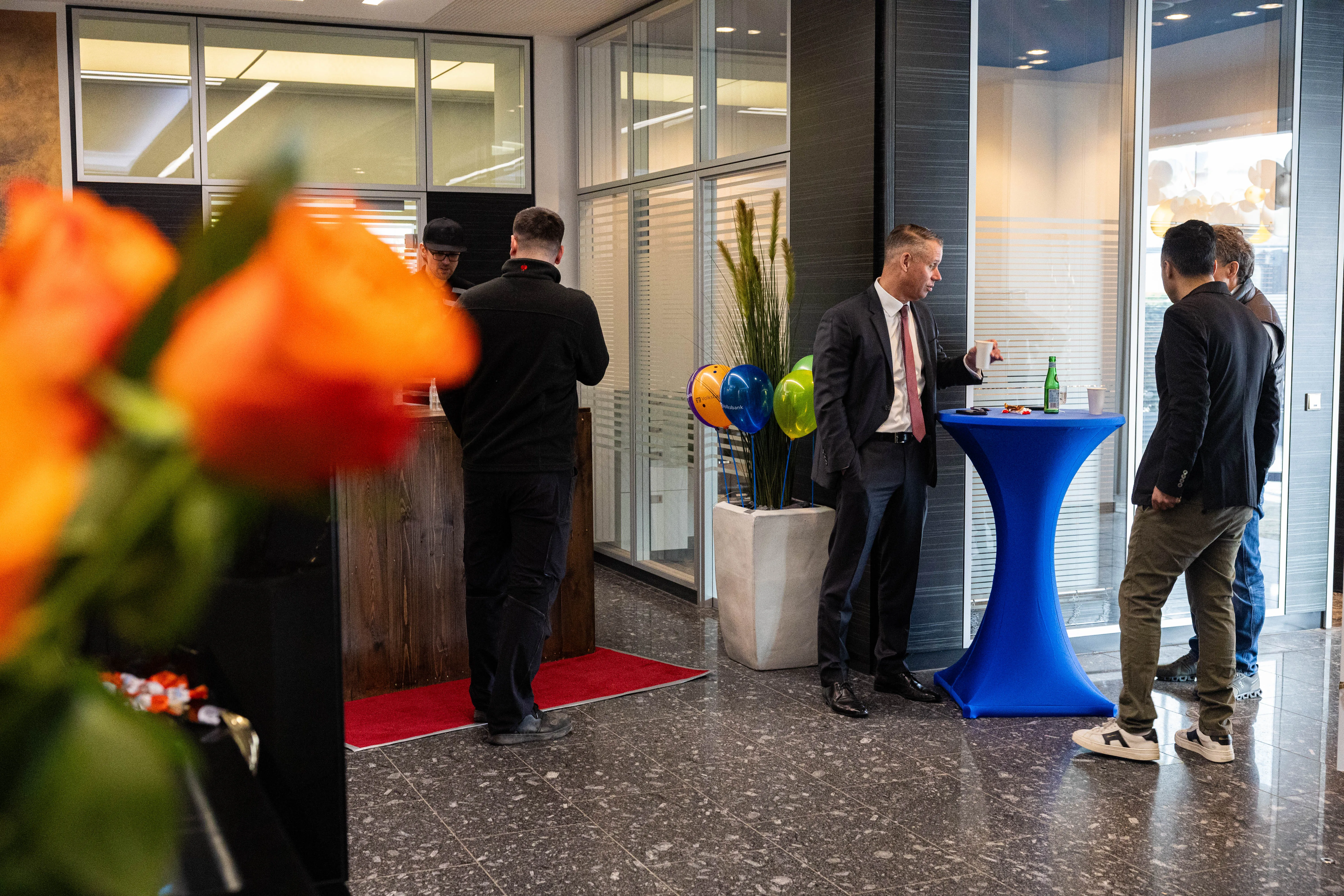 Drei Männer unterhalten sich auf einer Jubiläumsfeier der Volksbank Kierspe, im Hintergrund ein Empfangstresen und Ballons.
