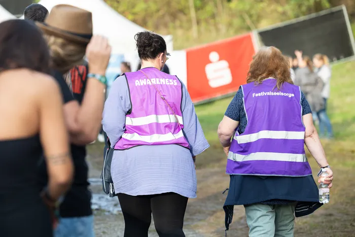 Zwei Personen in lila Westen mit den Aufschriften „AWARENESS“ und „Festivalseelsorge“ auf einem Festivalgelände.